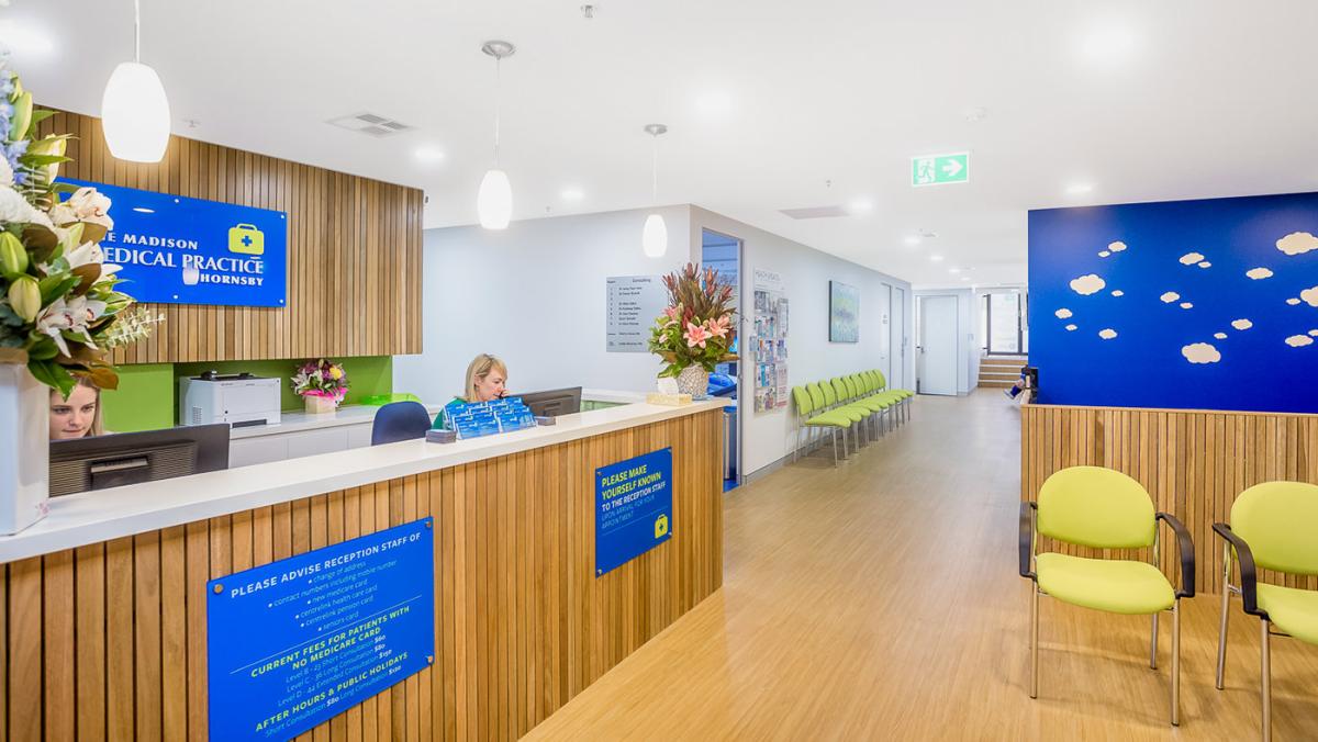 Modern medical practice reception area with wood panelling, green chairs and blue branding at Madison Medical