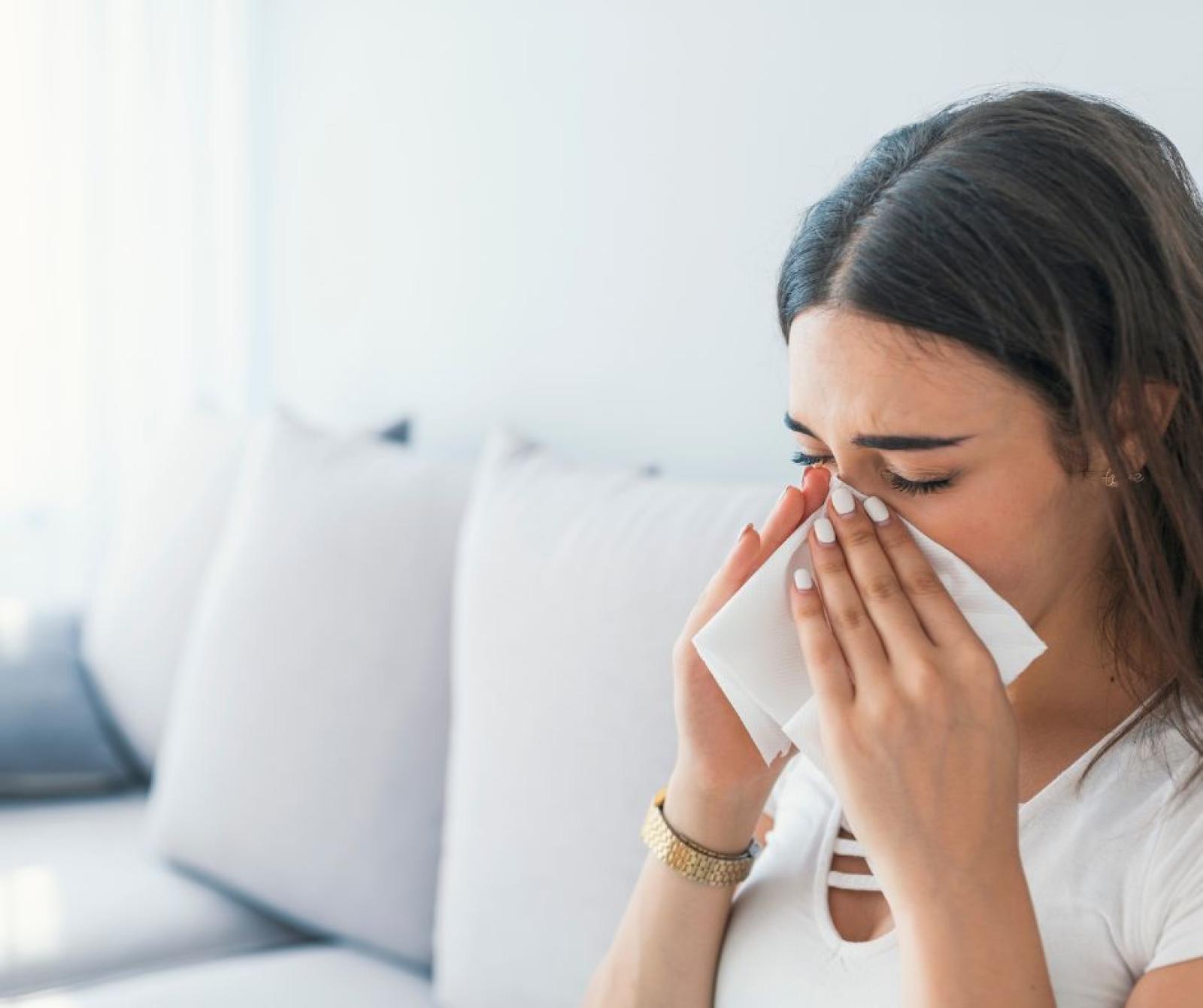 Woman holding tissue to face experiencing cold or allergy symptoms