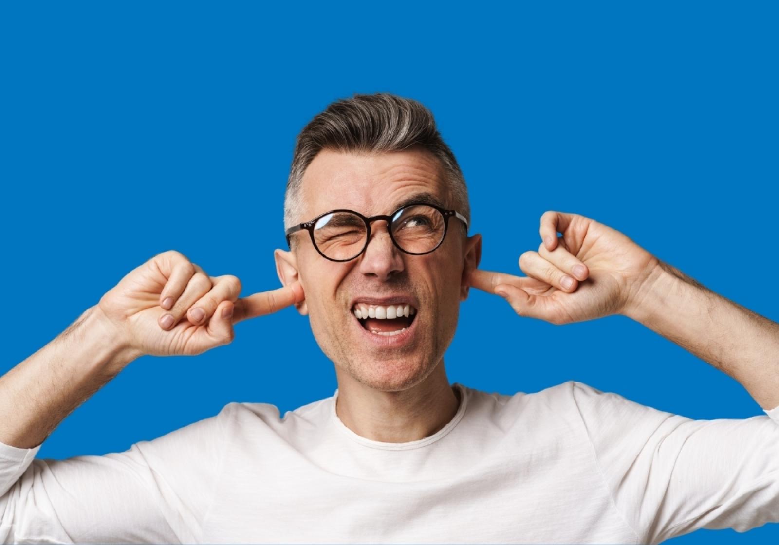 Man with glasses plugging ears and smiling against blue background