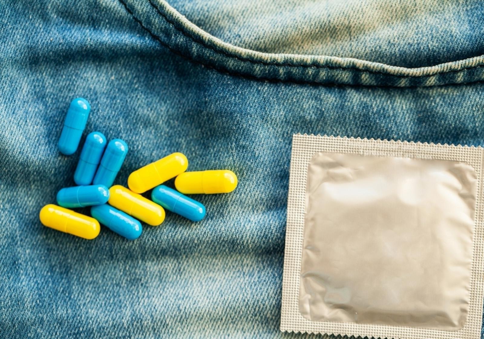 Blue and yellow capsule medications alongside a foil-wrapped contraceptive condom on blue fabric