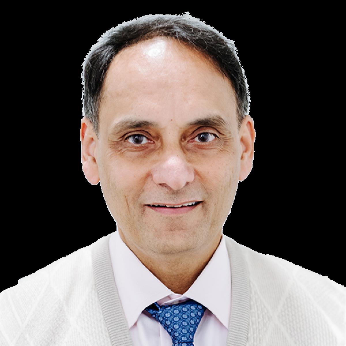 Professional headshot of male doctor in white coat with blue patterned tie smiling at camera