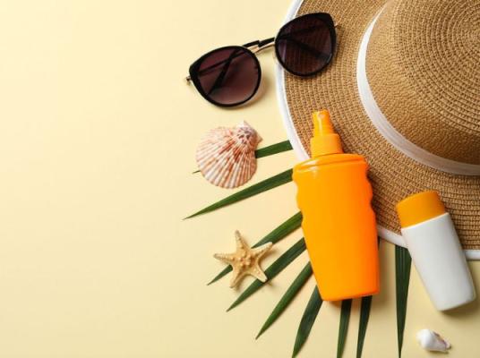 Sunscreen bottles and sunglasses arranged with tropical beach accessories on a cream background