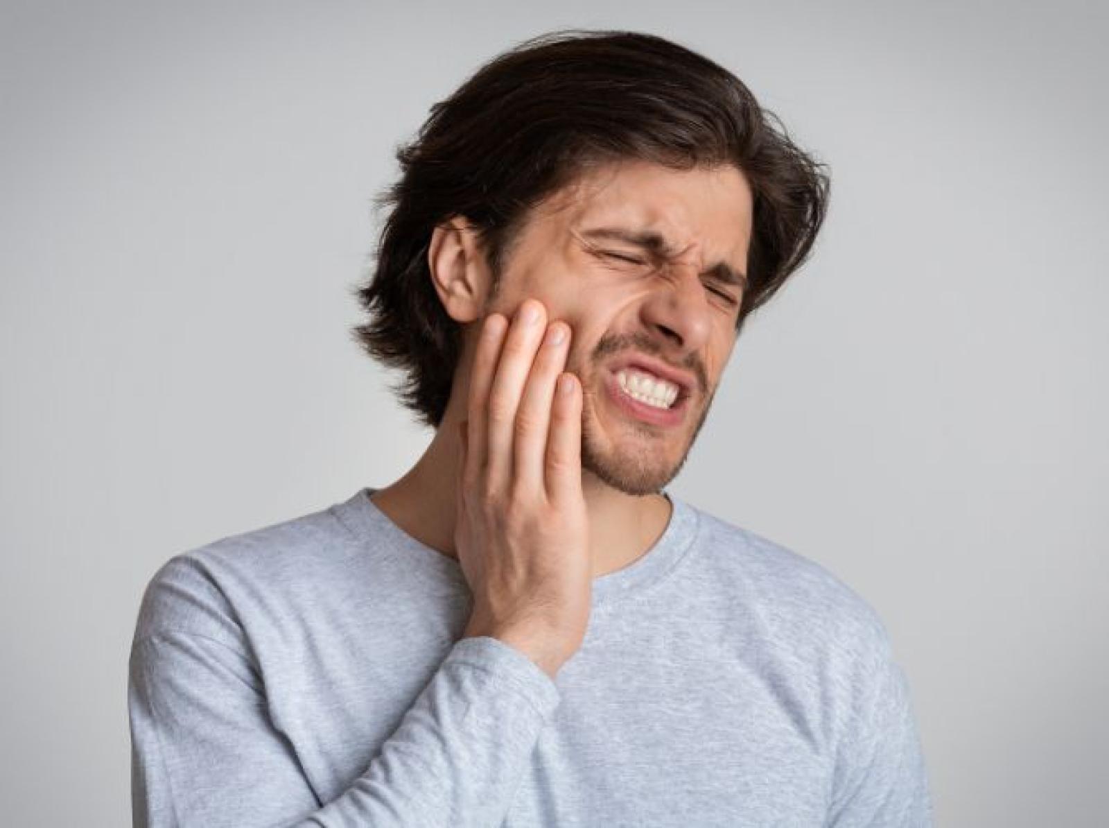 Man experiencing tooth or jaw pain, holding cheek with hand and grimacing