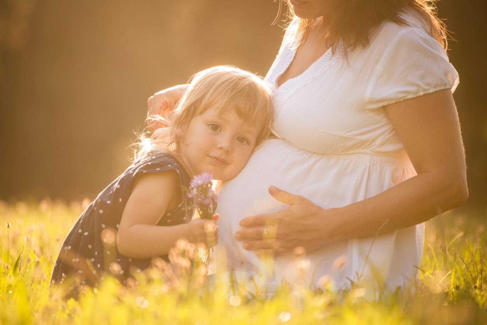 Pregnant woman holding toddler in sunny field, expecting mother with child