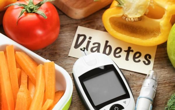 Blood glucose meter surrounded by fresh vegetables and a pen, illustrating diabetes management and healthy eating