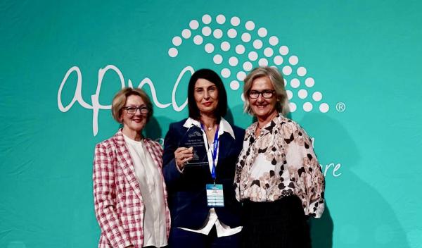 Three healthcare professionals at a medical conference holding an award in front of a teal branded backdrop